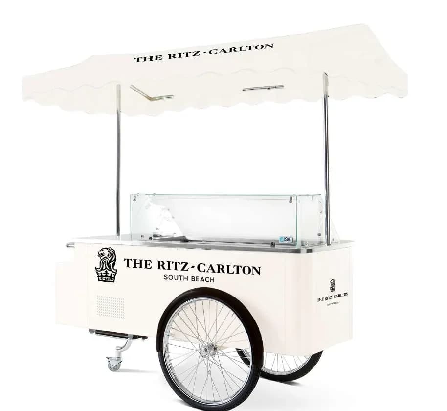 Cream-coloured Gelato-Go gelato cart with a scalloped canopy printed THE RITZ-CARLTON SOUTH BEACH, a glass display case and spoked wheels