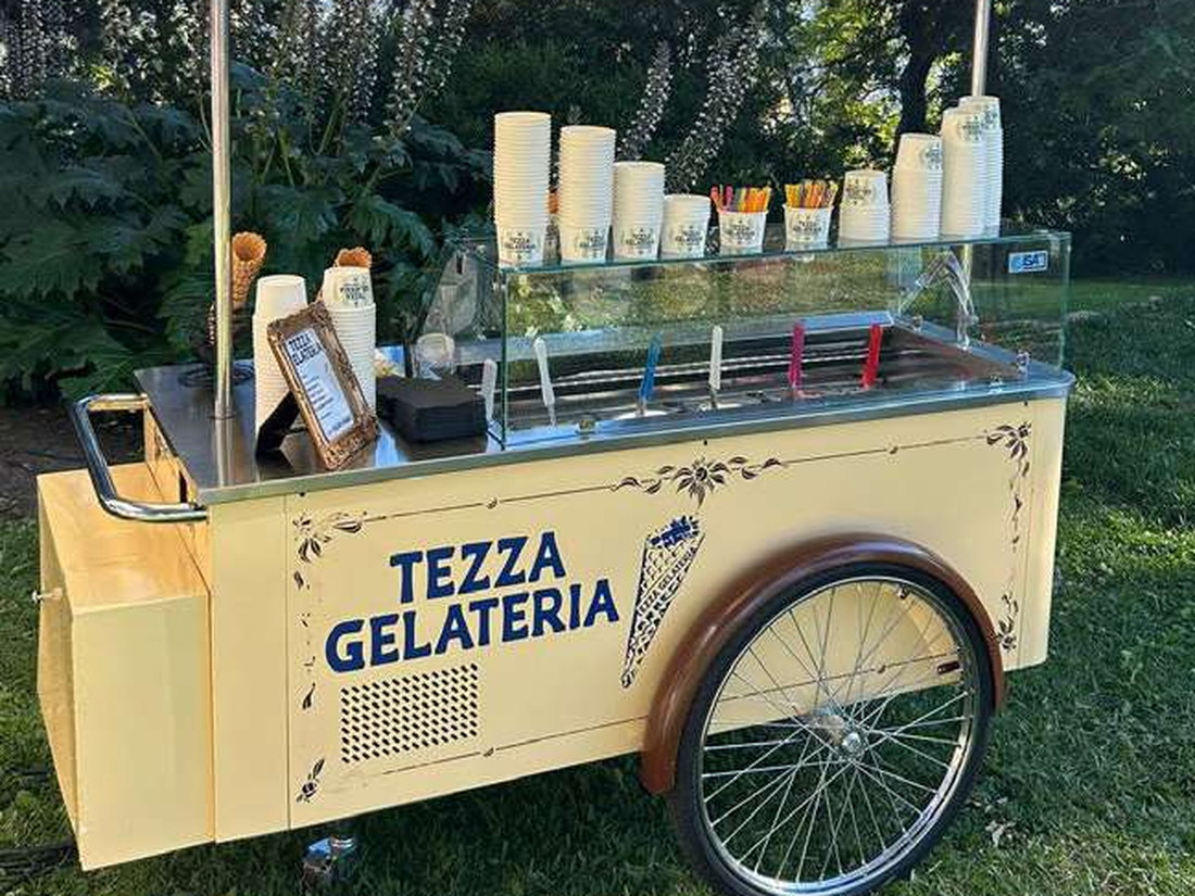 The Cart — the cream vintage Gelato Go cart with striped awning, gelato display and spoked wheel, set up on a lawn